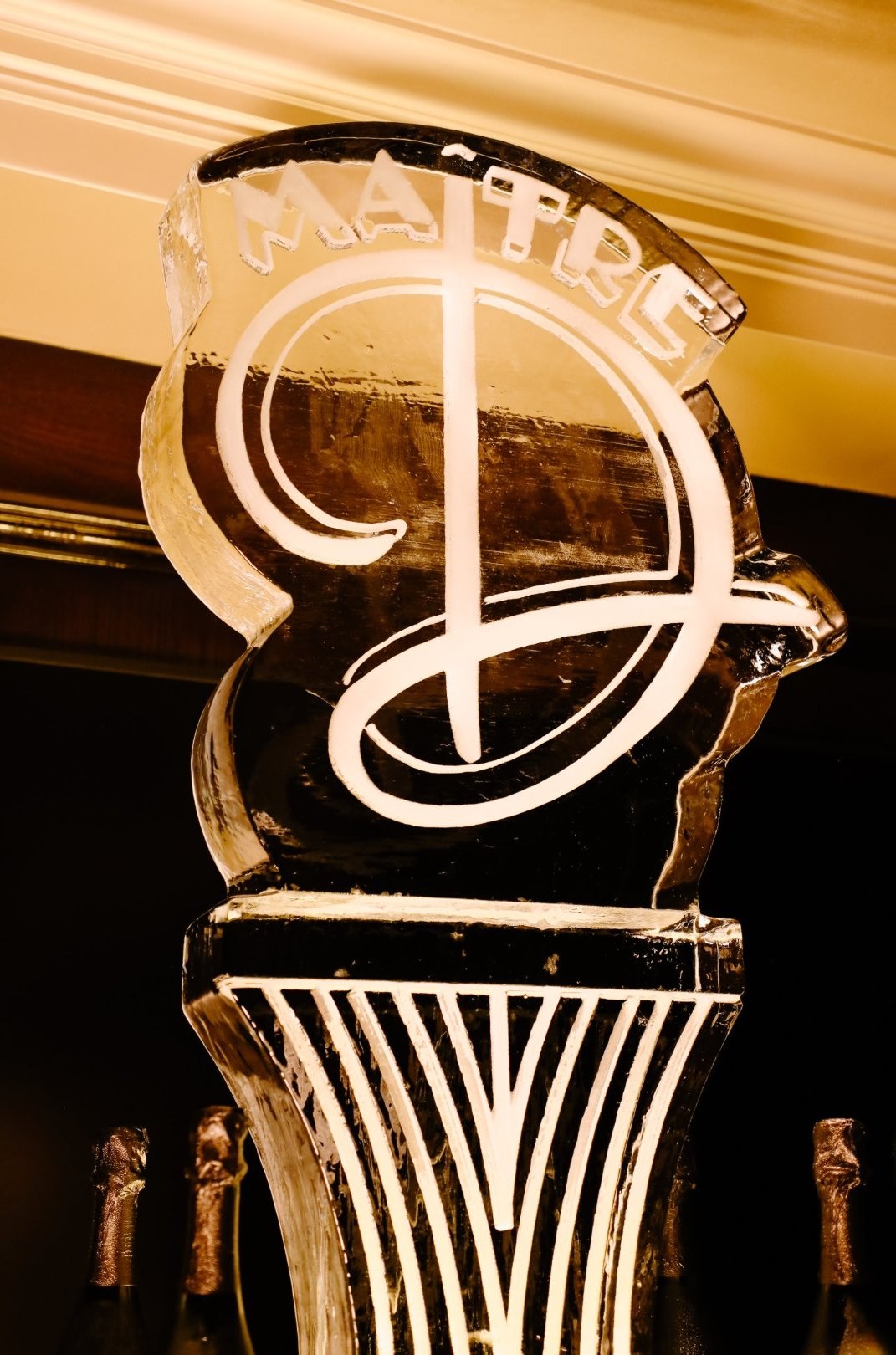 Ice sculpture carved with the Maître D monogram, glowing under warm light