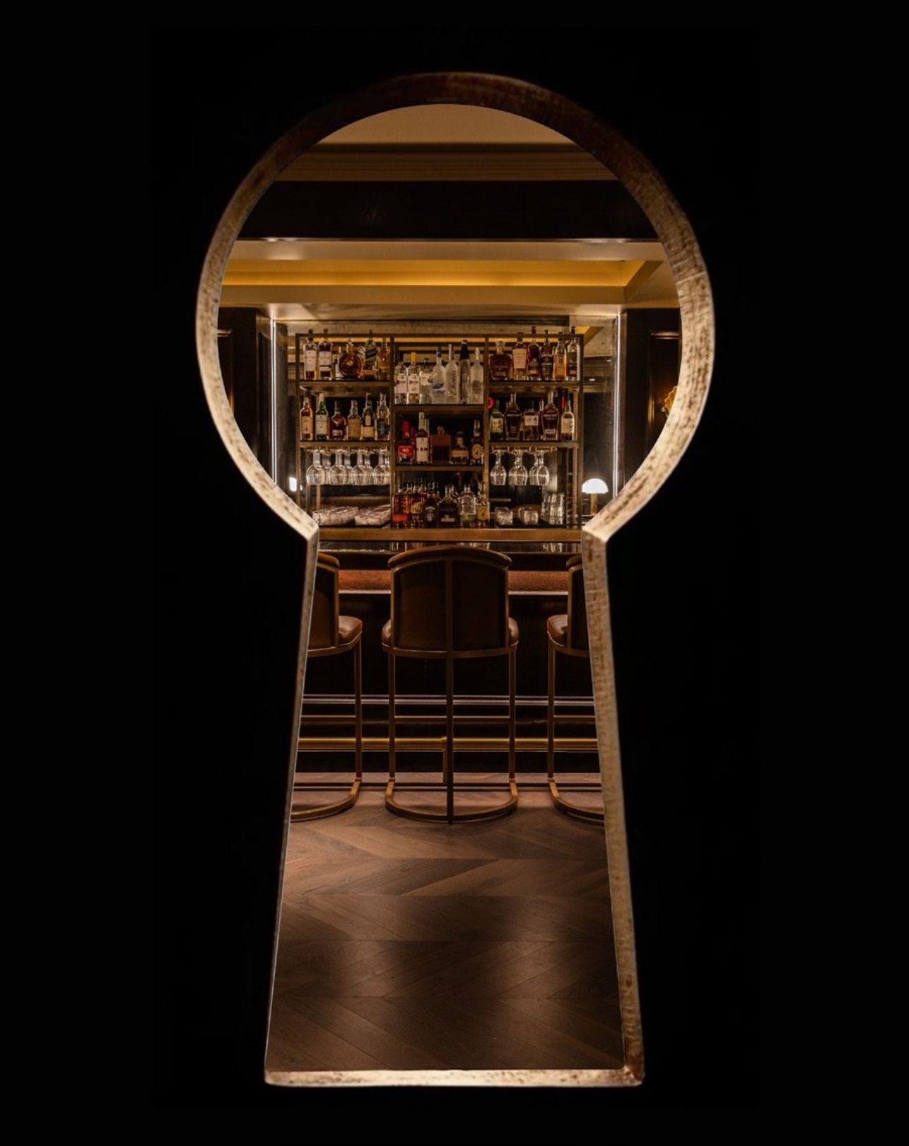 A view through a brass keyhole into the Maître D bar, lined with bottles and leather stools